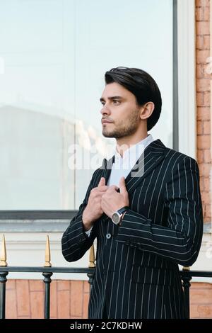 Giovane e attraente bruna con bearded uomo in camicia bianca e giacca classica a righe guardando da parte in piedi sulla strada della città Foto Stock