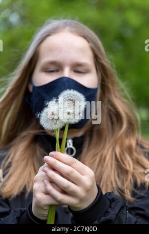 Scolastica con una maschera che tiene diversi dandelions Foto Stock