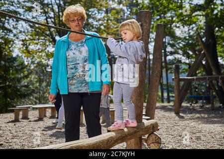 Bambina che gioca nel parco giochi sotto la supervisione di sua nonna Foto Stock