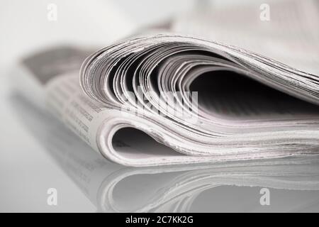 Giornale piegato a specchio su un tavolo di vetro su fondo piano con profondità di campo ridotta Foto Stock