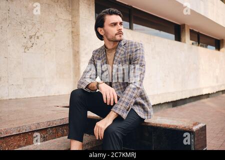 Giovane bell'uomo in elegante giacca a scacchi che guarda lontano all'aperto Foto Stock
