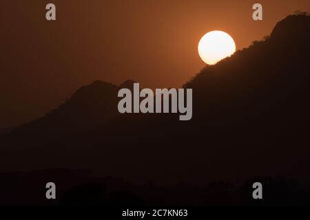 Un magico primo piano del sole che si abbassa dietro le montagne Foto Stock