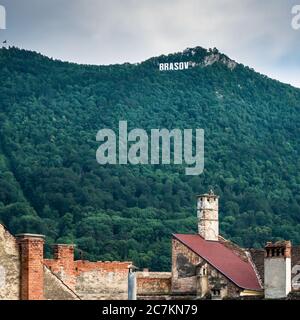 Brasov/Romania - 06.28.2020: Brasov scritto con lettere grandi sul Monte Tampa. Cartello Brasov con vecchi tetti e camini in primo piano Foto Stock