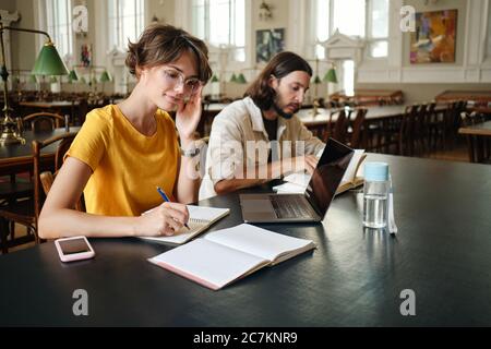 Due giovani studenti che fanno appunti di studio con il laptop in biblioteca di università Foto Stock
