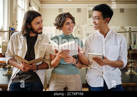 Gruppo di giovani studenti multinazionali molto interessanti che studiano felicemente in biblioteca Foto Stock