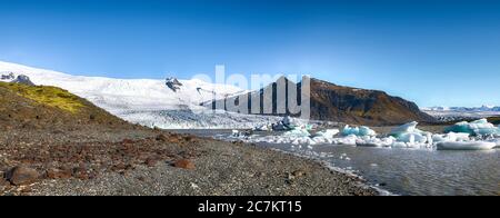 Vista panoramica degli iceberg che si fondono galleggianti nel lago glaciale di Fjallsarlon con il ghiacciaio di Fjallsjokull che calpita in laguna sullo sfondo. Luogo: FJA Foto Stock