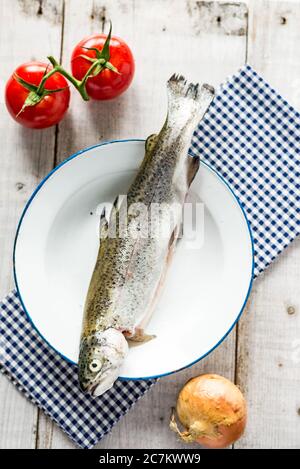 Trota fresca dal mercato su un piatto marittimo con due pomodori rossi e una cipolla, su un panno controllato Foto Stock