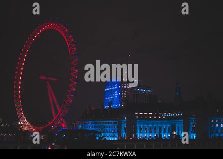Inquadratura grandangolare del London Eye rosso accanto a. un edificio di notte Foto Stock