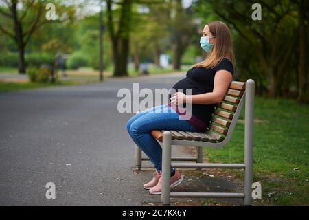 Donna incinta seduta su una panchina del parco a Spadtpark in primavera, crisi corona, (CoVID-19), Baviera, Germania Foto Stock