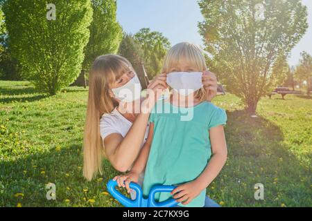 Madre mette sulla maschera di faccia su figlia, Stadtpark, crisi di Corona, Ratisbona, Baviera, Germania Foto Stock