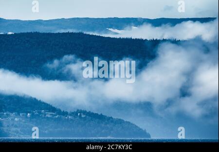 Ampio scatto di una catena montuosa con nebbia e un piccola città sotto in una giornata fredda Foto Stock