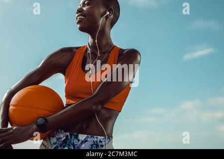 Sportivo all'aperto con un basket. Donna con un basket che guarda via e sorridente contro il cielo. Foto Stock