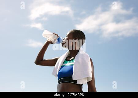 Donna fitness che beve acqua contro il cielo. Atleta femmina che beve acqua all'aperto dopo la sessione di allenamento. Foto Stock