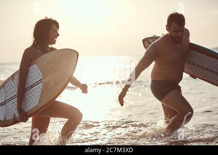 giovane coppia caucasica che esce dall'acqua, sorridente, tiene tavole da surf Foto Stock