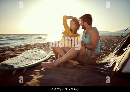 giovane coppia caucasica che si inonda al tramonto in spiaggia, seduta insieme in spiaggia con gambe intrecciate, coccolandosi. spazio copia Foto Stock