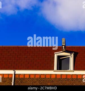 Tetto rosso con una finestra a mansarda bianca contro un cielo blu Foto Stock