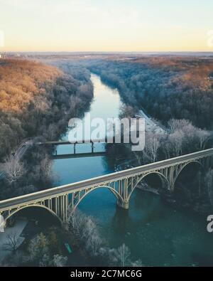 Un lungo colpo di un fiume fiancheggiato da alberi autunnali e. un ponte ad arco in primo piano Foto Stock