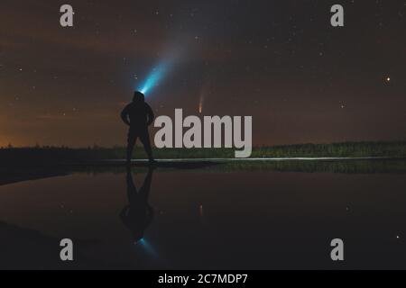 Guy nel cappuccio brilla una lanterna e guarda la cometa Neoswise Foto Stock