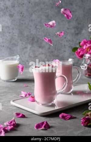 Latte di luna di rosa in tazze di vetro e petali di rosa cadenti su sfondo grigio. Primo piano. Foto Stock