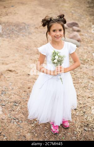 una bambina tiene un bouquet di fiori bianchi in rosa sneakers.dark capelli, fiori bianchi nelle mani, vestito bianco Foto Stock