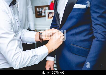 Il primo colpo di groomsman aiuta lo sposo ad abbellire il suo vestito Foto Stock