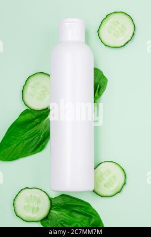 vasetto cosmetico bianco con fette di cetrioli e foglie fresche su uno sfondo di menta chiara. primo piano, copia spazio, mock up Foto Stock