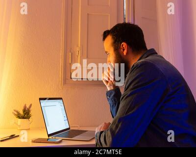 Uomo sopportato seduto e guardando qualcosa sul suo laptop Foto Stock