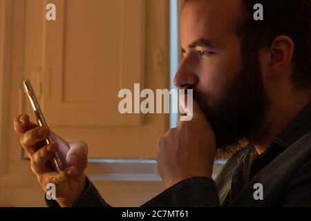 Uomo bearded guardando il suo telefono in mano e. pensare a qualcosa Foto Stock
