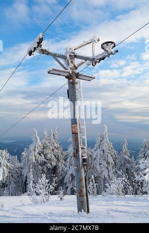 Vecchio e arrugginito palo di traino da sci - dispositivo per il trasporto in stazione sciistica. Il meccanismo è circondato dalla natura invernale Foto Stock