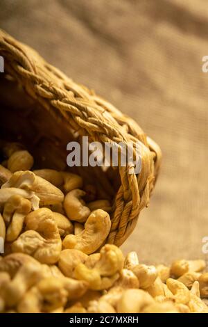 Noci di anacardi in un cesto di vimini e noci di anacardi sparse su tela di tela con una superficie di tessitura ruvida. Primo piano Foto Stock