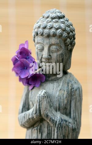 Primo piano di una statua di Buddha con fiori di petalo viola Foto Stock