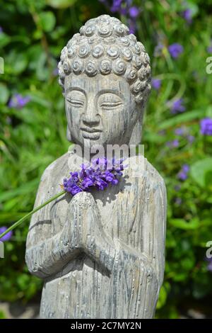 Primo piano di una statua di Buddha con fiori di petalo viola Foto Stock