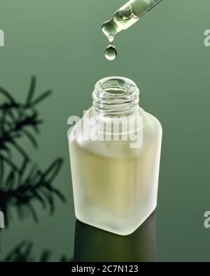 Una goccia di olio essenziale che cade da una pipetta in una bottiglia su sfondo verde Foto Stock