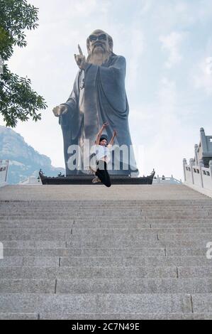 Una donna cinese che si diverte e salta sulle scale che conducono a Laozhi, filosofo cinese, all'interno della zona panoramica del Palazzo di Taiqing a Qingdao Cina Foto Stock