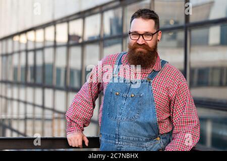 Ritratto di bruto artigiano alla moda con la bruta tuta blu, camicia controllata in stile vintage della metà del 20 ° secolo, guardando la fotocamera, all'aperto Foto Stock