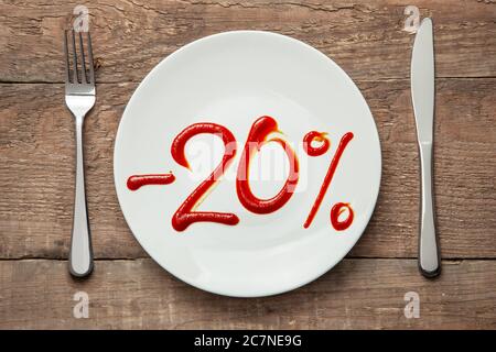 20 di sconto sul cibo. Vendita di cibo. Piastra con l'iscrizione ketchup e forchetta con coltello su tavola di legno. Foto Stock