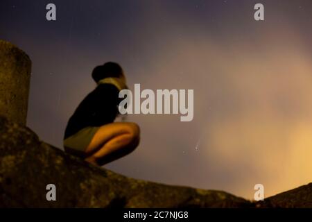 Una ragazza è vista guardare la Comet NEOWISE o C/2020 F3 dopo il tramonto con nuvole di fumo a causa dei forti incendi intorno alla città di Porto, Portogallo. Il 18 luglio 2020. - sul retro della ragazza anche aar una stella di tiro lasciando la sua traccia os l'immagine. Foto Stock