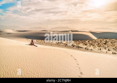 Giovane donna ragazza sulla sabbia in dune bianche monumento nazionale in New Mexico seduta su slitta disco per scivolare giù collina durante il tramonto vintage tono Foto Stock