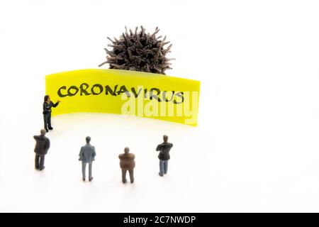 Incontro con statuette in miniatura poste come uomini d'affari in piedi intorno post-it nota con Coronavirus scritto a mano messaggio in background, minimalista Foto Stock