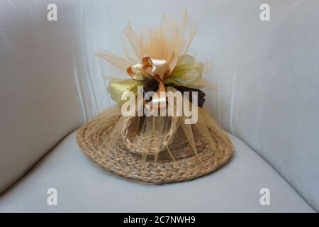 Colpo di closeup di un cappello di paglia avvolto in tessuto tulle e legato con un nastro su uno sfondo bianco Foto Stock