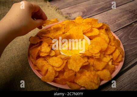 La ragazza prende un chip da un piatto rotondo con patatine e una pentola con salsa di formaggio al centro del piatto. Primo piano Foto Stock