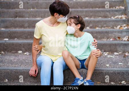 Madre e figlia di mezza età siedono sulla strada indossando maschere Foto Stock