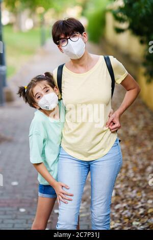 Madre e figlia di mezza età in piedi sulla strada indossando maschere Foto Stock