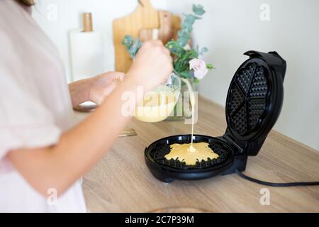 primo piano di mani femminili che versano l'impasto grezzo alla macchina per waffle Foto Stock