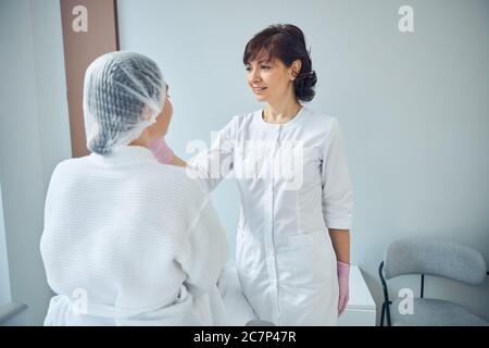 Gioioso operatore medico che controlla la pelle del viso del paziente Foto Stock