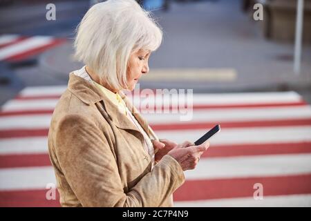 Bella donna caucasica anziana che guarda sullo schermo del telefono Foto Stock