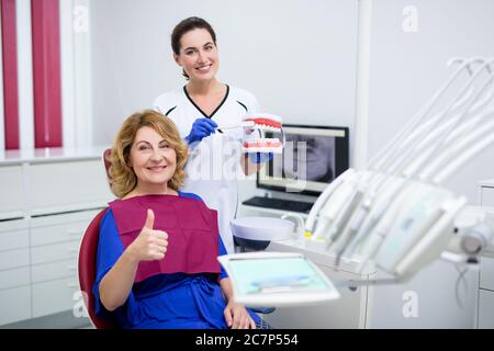 attraente medico femminile con spazzolino da denti e mascelle artificiali e paziente donna matura Foto Stock