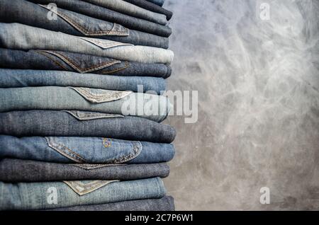 Una pila di jeans da donna piegati con precisione su sfondo grigio. Primo piano di jeans in diversi colori. Jeans texture o sfondo denim. Spazio di copia Foto Stock