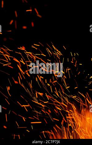 Scintille rosse che bruciano su uno sfondo nero. Particelle incandescenti di arancio fiero che volano via nel cielo notturno. Spazio di copia. Sfondo astratto Foto Stock