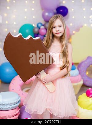 ritratto di carina bambina che tiene enorme gelato con gigantesco pasticceria decorazioni sfondo Foto Stock